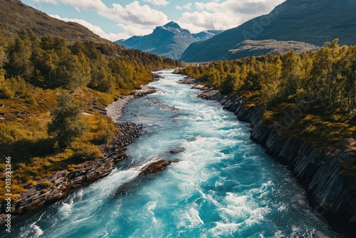 Drone high-angle photo of the turquoise-colored mountain river flowing in the pine woodland with a view of the mountain peaks in the background in Innlandet County, Norway photo