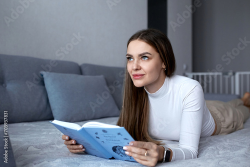 Beautiful sexy adult woman spends her weekend in a comfortable bedroom, lying on the bed, reading a book and enjoying classic literature.