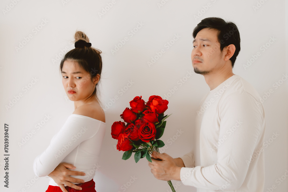 Asian man giving red rosed and flirting, begging for love on valentines day, apologizing woman dislike and ignoring, both standing isolated over white background wall. Asian man giving red rosed and flirting, begging for love on valentines day, apologizing woman dislike and ignoring, both standing isolated over white background wall.