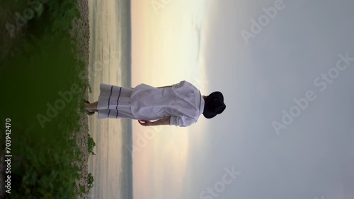 A young woman in a hat standing on the seashore looking into the distance beyond the horizon against the background of a cloudy sky. Summer vacation concept photo