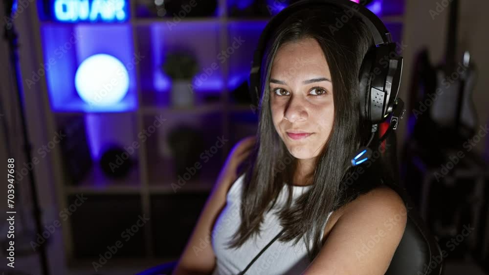 Young beautiful hispanic woman streamer sitting on table with serious face at gaming room Young beautiful hispanic woman streamer sitting on table with serious face at gaming room