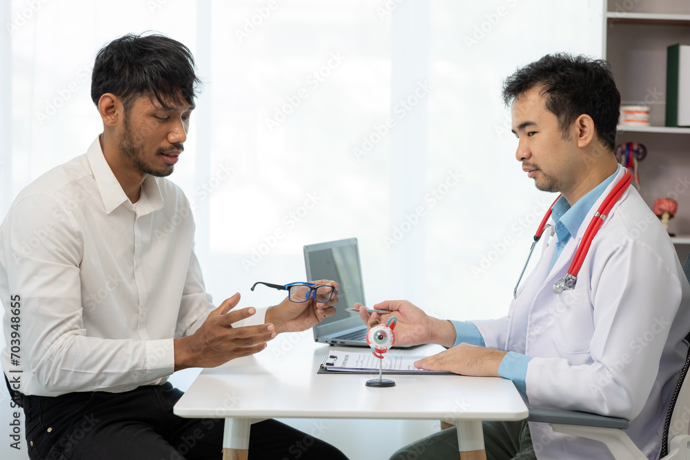 Close-up of an Asian male doctor showing an eyeball model and explaining eye diseases to a male patient in hospital. health care concept Close-up of an Asian male doctor showing an eyeball model and explaining eye diseases to a male patient in hospital. health care concept