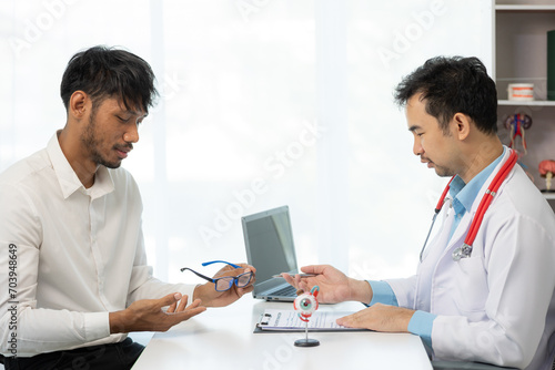 Close-up of an Asian male doctor showing an eyeball model and explaining eye diseases to a male patient in hospital. health care concept