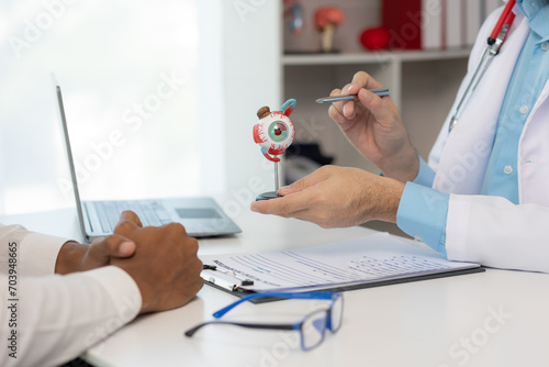 Close-up of an Asian male doctor showing an eyeball model and explaining eye diseases to a male patient in hospital. health care concept photo