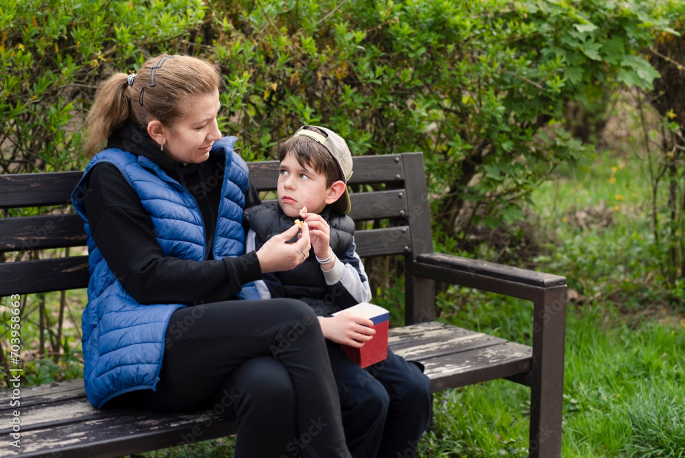 A mother and her son talk in the park and eat popcorn, the boy is sad, the mother tries to explain to son that he was naughty and offended younger boy A mother and her son talk in the park and eat popcorn, the boy is sad, the mother tries to explain to son that he was naughty and offended younger boy