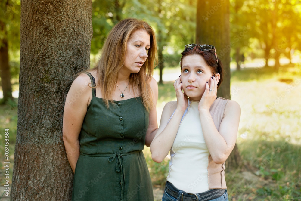 Fototapeta premium The teenage girl got tired of listening to mother and closed ears, the girl constantly hears criticism and notations from her parents. Mother and teenage daughter are talking in the park