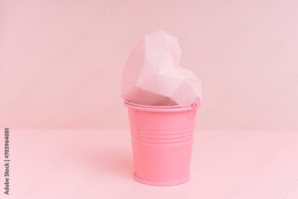 Pink paper heart in a bucket against a pink background. Pink paper heart in a bucket against a pink background.