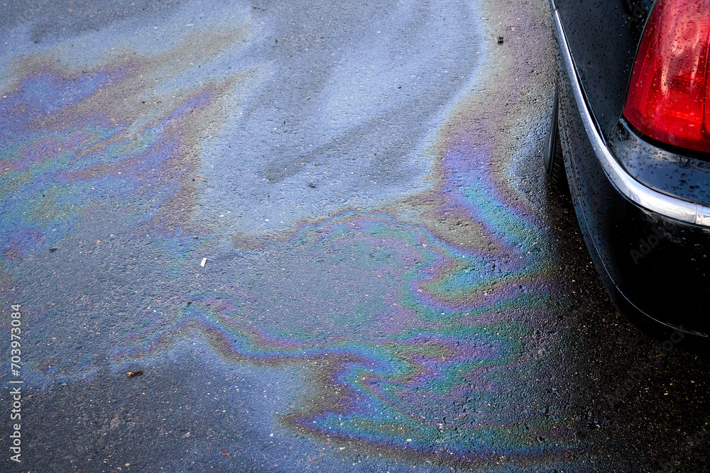 Obraz premium Leakage of oil or gasoline from the car on the asphalt in the parking lot.