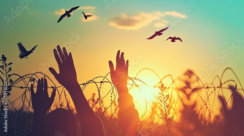 Human right day concept: Silhouette refugee hands raising with birds flying and barbed wire on autumn sunset background  photo