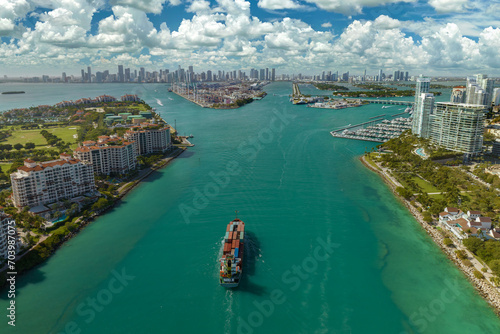 Aerial view of large container ship entering in Miami harbor main channel near South Beach. Luxurious hotels and apartment buildings on waterfront and high skyscrapers of downtown district in distance photo
