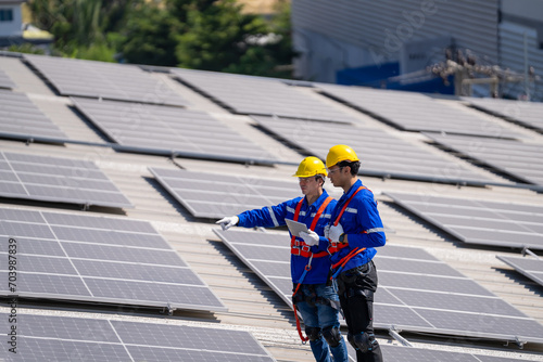 Specialist technician professional engineer checking top view of installing solar roof panel on the factory rooftop under sunlight. Engineers having service job of electrical renewable eco energy