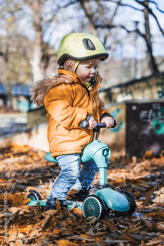 Adorable toddler boy wearing yellow protective helmet riding baby scooter outdoors on autumn day. Kid training balance on mini bike in city park. Fun autumn outdoor activity for small kids © kasto