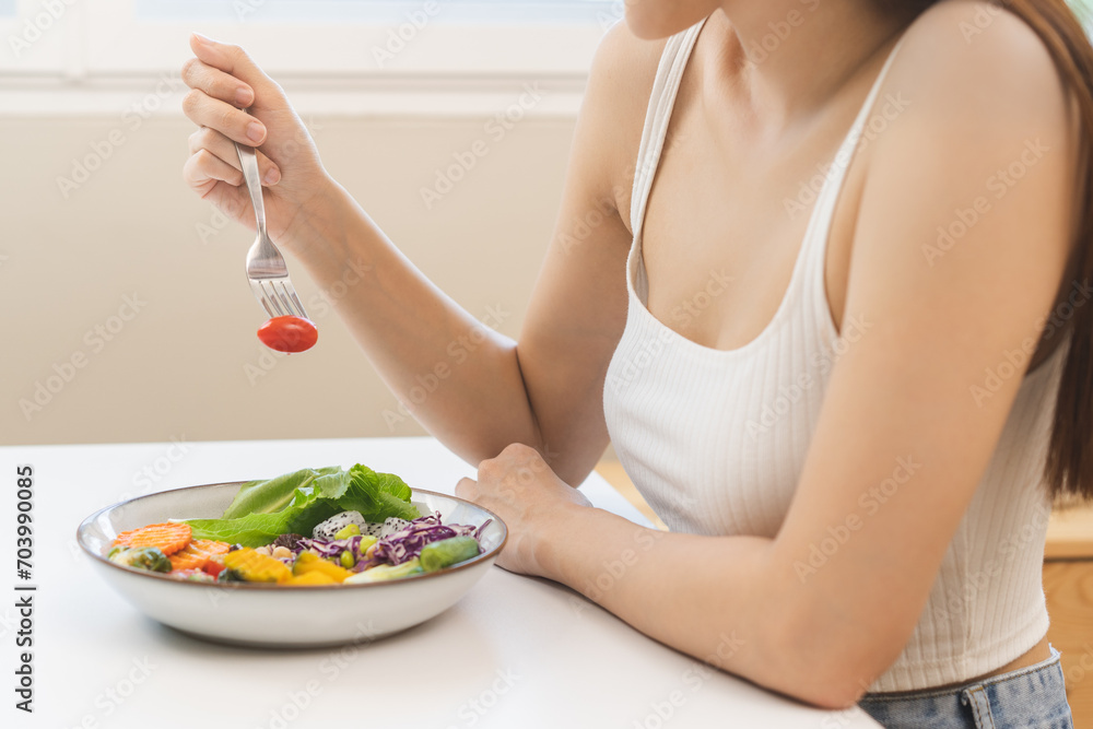 Diet concept, close up young woman hand use a fork to prick the tomato, fresh vegetable or green salad, eat nutrition food  on table at home, low fat to good body. Girl getting weight loss for healthy