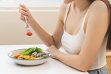Diet concept, close up young woman hand use a fork to prick the tomato, fresh vegetable or green salad, eat nutrition food  on table at home, low fat to good body. Girl getting weight loss for healthy
