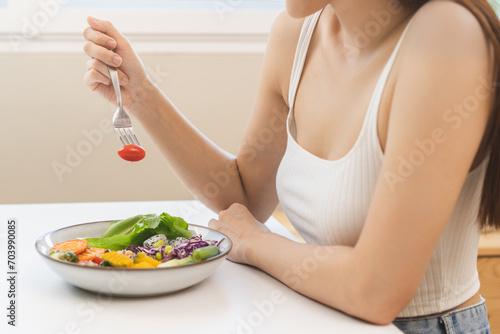 Diet concept, close up young woman hand use a fork to prick the tomato, fresh vegetable or green salad, eat nutrition food on table at home, low fat to good body. Girl getting weight loss for healthy