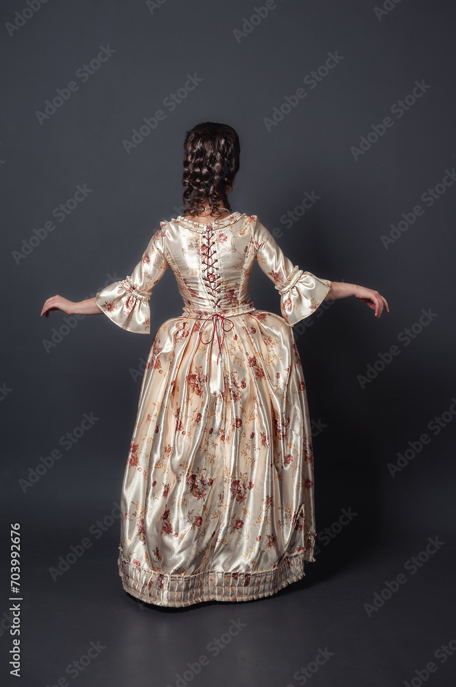 Beautiful woman in rococo style medieval dress against dark background back pose
