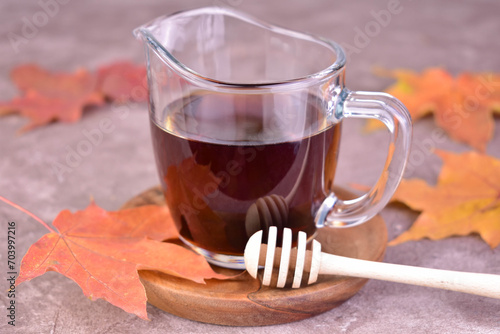 Maple syrup in a glass gravy boat on a gray background and clon leaves.
