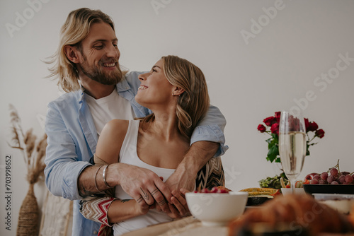 Young loving couple embracing and smiling while enjoying romantic dinner at home together