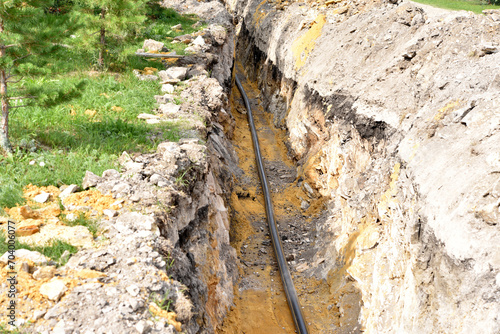 A plastic black gas pipe at the bottom of the trench. A dug trench for laying a gas pipe.