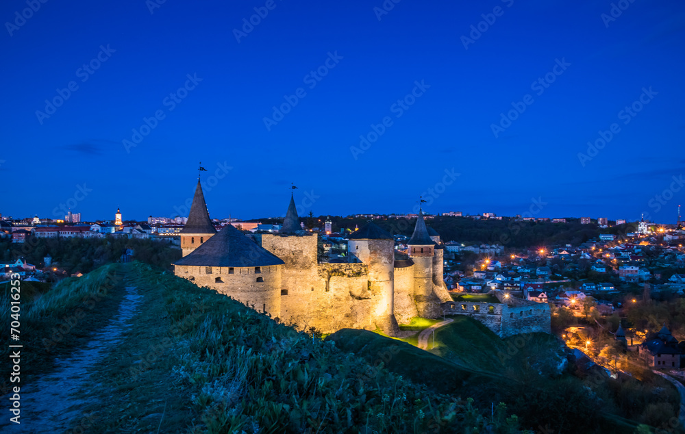 View on the Kamianets-Podilskyi Castle in the evening. Beautiful stone castle on the hill on the sunset. Clouds in the darkening sky above the castle. Blue hour. Ukraine