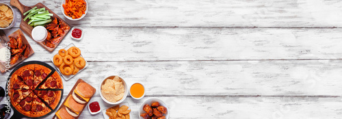 Junk food corner border. Pizza, hamburgers, chicken wings and salty snacks. Top down view over a white wood banner background.