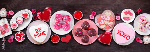 Valentines Day table scene with an assortment of fun desserts and sweets. Overhead view on a dark wood banner background. Love and hearts theme.