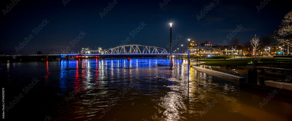 Colourful decoration on steel draw bridge in the background with high water levels of river IJssel flooded countenance boulevard of tower town Zutphen at nighttime with street lights