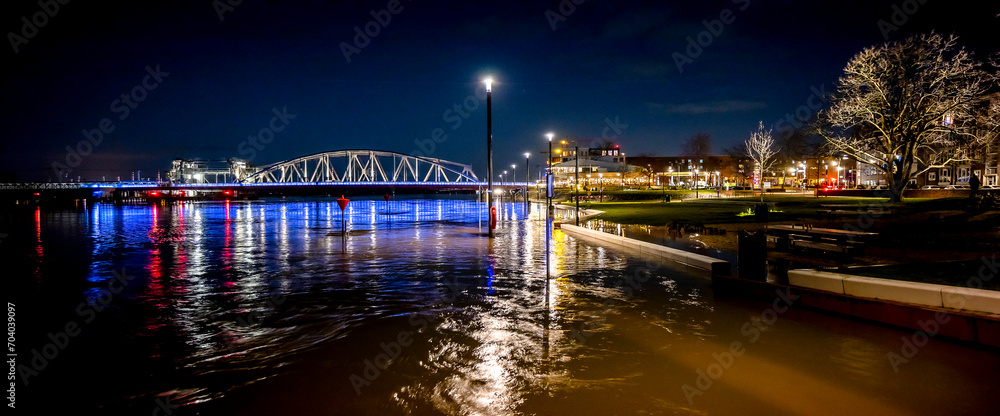 Colourful decoration on steel draw bridge in the background with high water levels of river IJssel flooded countenance boulevard of tower town Zutphen at nighttime with street lights
