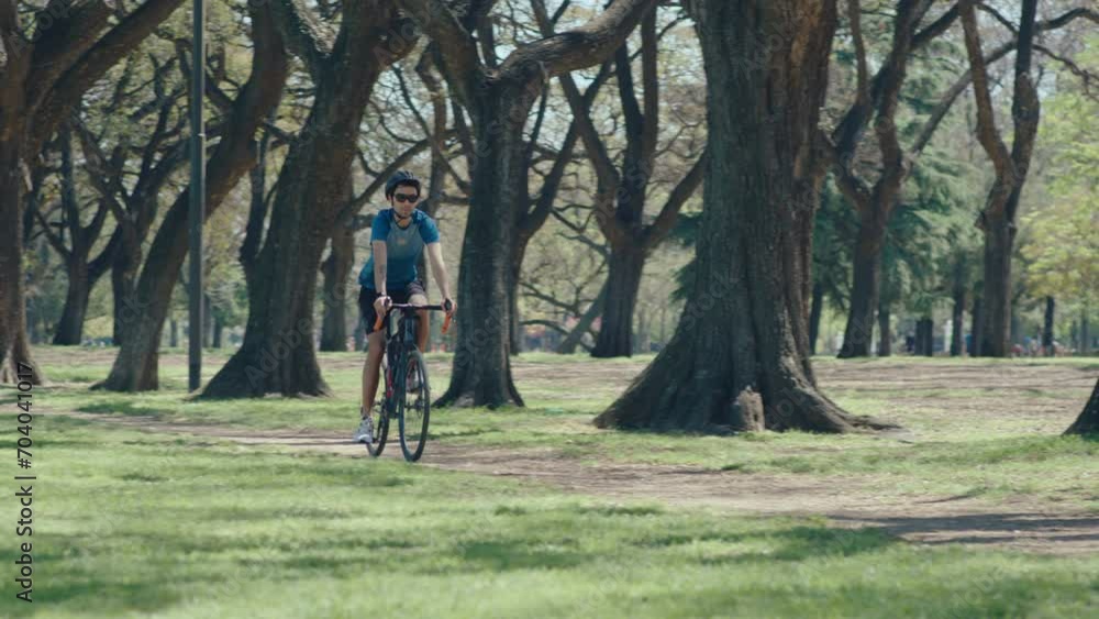 Young cyclist in sunglasses, bike helmet and sports clothing riding a road bicycle on path in public park on summer day when spending weekend day outdoors Young cyclist in sunglasses, bike helmet and sports clothing riding a road bicycle on path in public park on summer day when spending weekend day outdoors