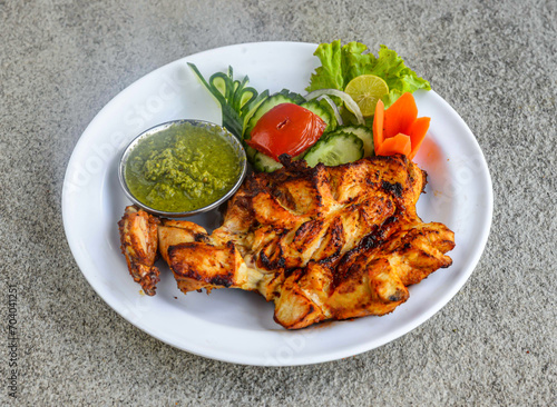 Grilled chicken breast tikka piece with chutney and salad served in dish isolated on grey background side view of indian spices and pakistani food