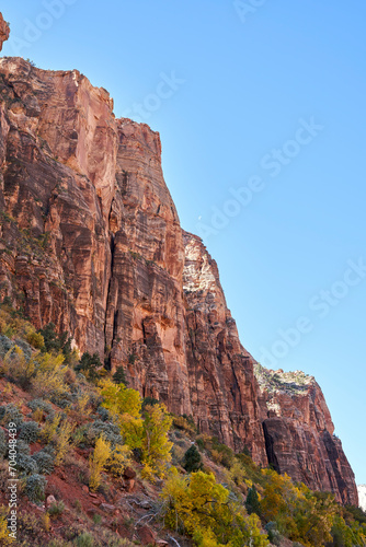 The steep mountain cliffs of zion national park. Blue sky is overhead, and barely seen in the distance is the moon