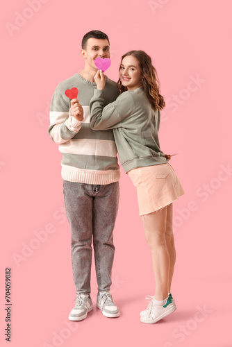 Funny young couple with paper hearts on pink background. Valentine's day celebration