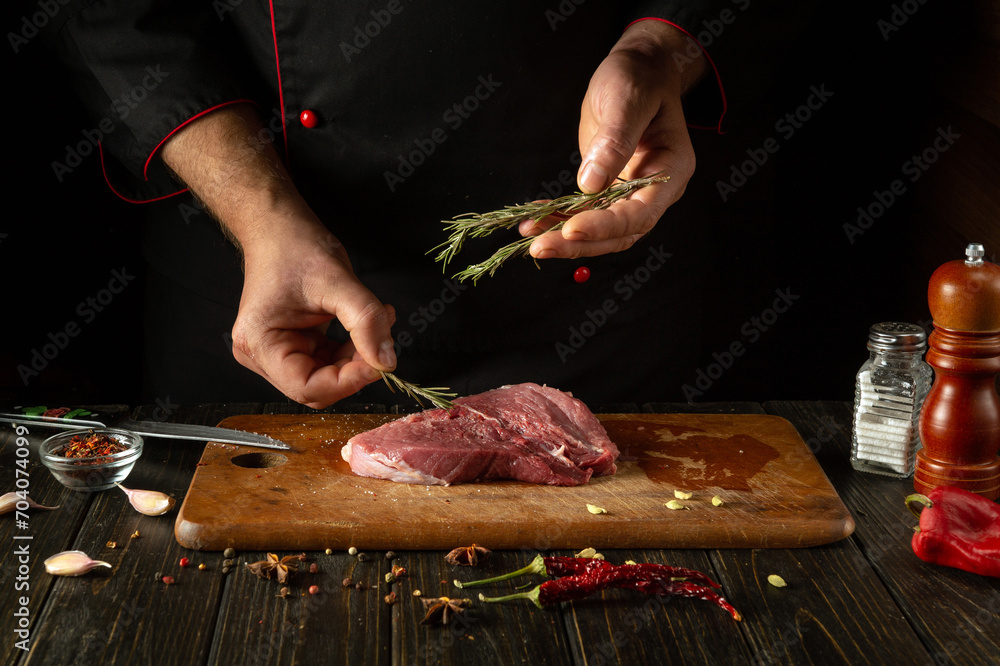 Adding rosemary to meat by the hand of the chef for aroma and taste. The process of cooking beef steak on the kitchen table with spices and pepper.