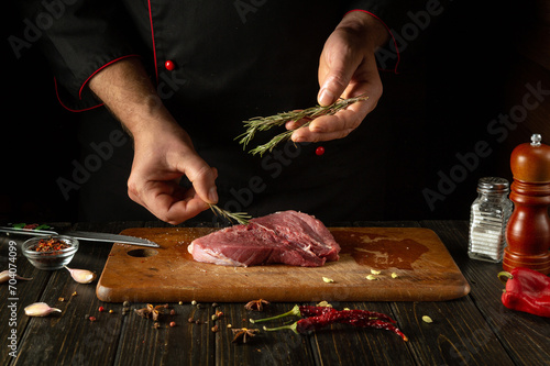 Adding rosemary to meat by the hand of the chef for aroma and taste. The process of cooking beef steak on the kitchen table with spices and pepper.