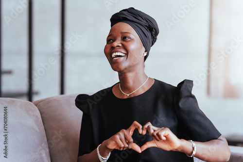 Photography Joyful woman in black turban and dress smiling and creating a heart shape with h