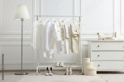 Rack with different stylish women`s clothes, shoes, lamp and dresser near white wall in room © New Africa