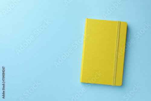 Closed yellow notebook on light blue background, top view. Space for text
