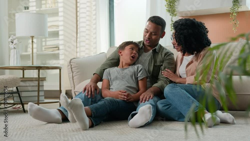 Happy multiracial family parents and joyful little boy kid son on floor laughing having fun African American mom dad talking with child celebrate relocation day weekend at home upbringing parenthood photo