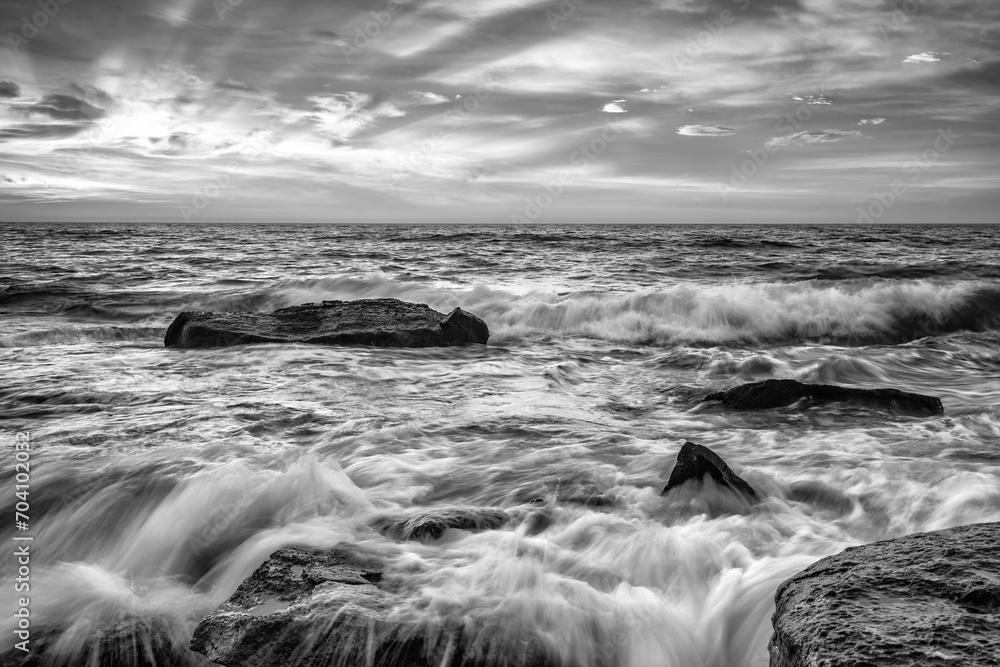 Stunning sunrise over the sea with the rocky sea coast in black and white.