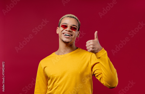 Positive man makes hand sign like, thumbs up gesture. Happy student guy on red