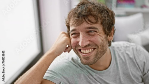 Handsome young man, chilling at home, confidently smiling and looking away. portrait of hispanic guy with beard, sitting on sofa, laughing naturally in cozy living room.