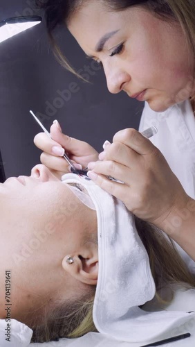 Close-up. Eyelash extension procedure with beauty salon . Makeup artist carefully increases eyelashes of client lying in front of her. Concept of beauty and fashion. Professional work. 4k footage.