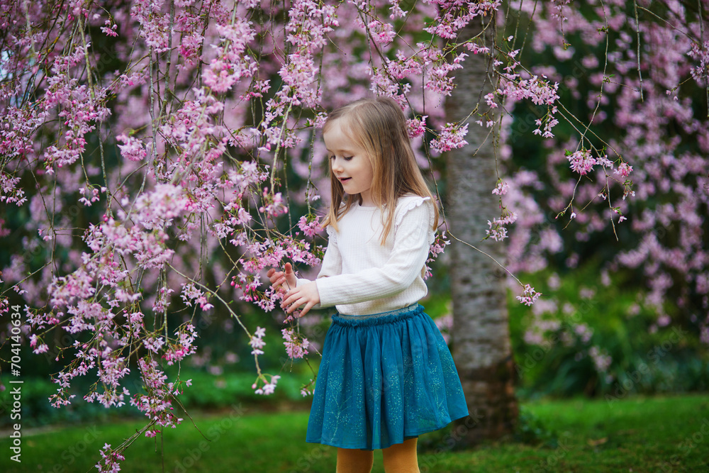 Adorable preschooler girl enjoying nice spring day in park during cherry blossom season Adorable preschooler girl enjoying nice spring day in park during cherry blossom season