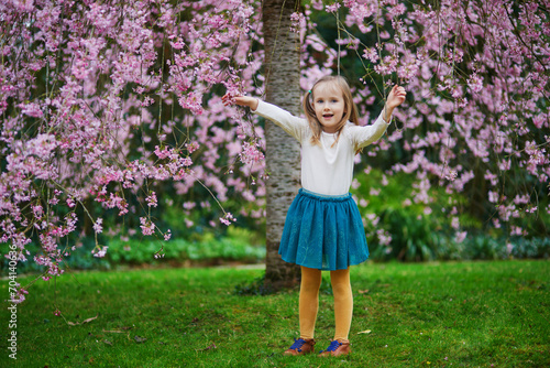 Adorable preschooler girl enjoying nice spring day in park during cherry blossom season