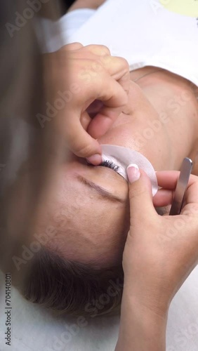 Stylist, cosmetologist glues white cosmetic patches under client's eyes before cosmetic procedure. Beauty salon. Concept of beauty and fashion. Professional work of stylist. 4k footage.