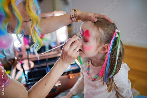 Artist painting little preschooler girl like unicorn on a birthday party. Creative activities for kids photo