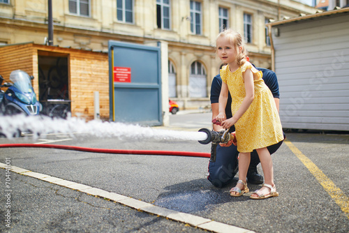 preschooler girl acting like a fireman holding firehose nozzle and splashing water photo