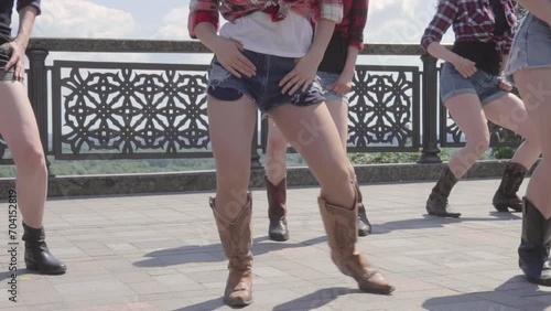 Several young girls dancing country line dance on the asphalt, USA style. Close up view to female hips and feet with brown cowboy country boots and jeans shorts. A little slow motion video