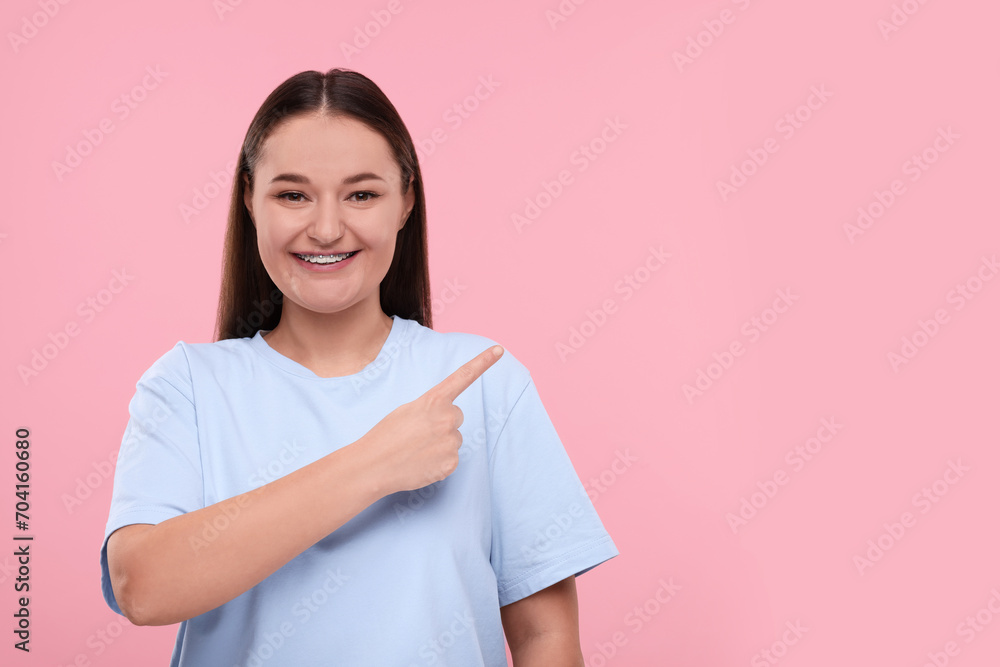 Smiling woman with dental braces pointing at something on pink background. Space for text Smiling woman with dental braces pointing at something on pink background. Space for text