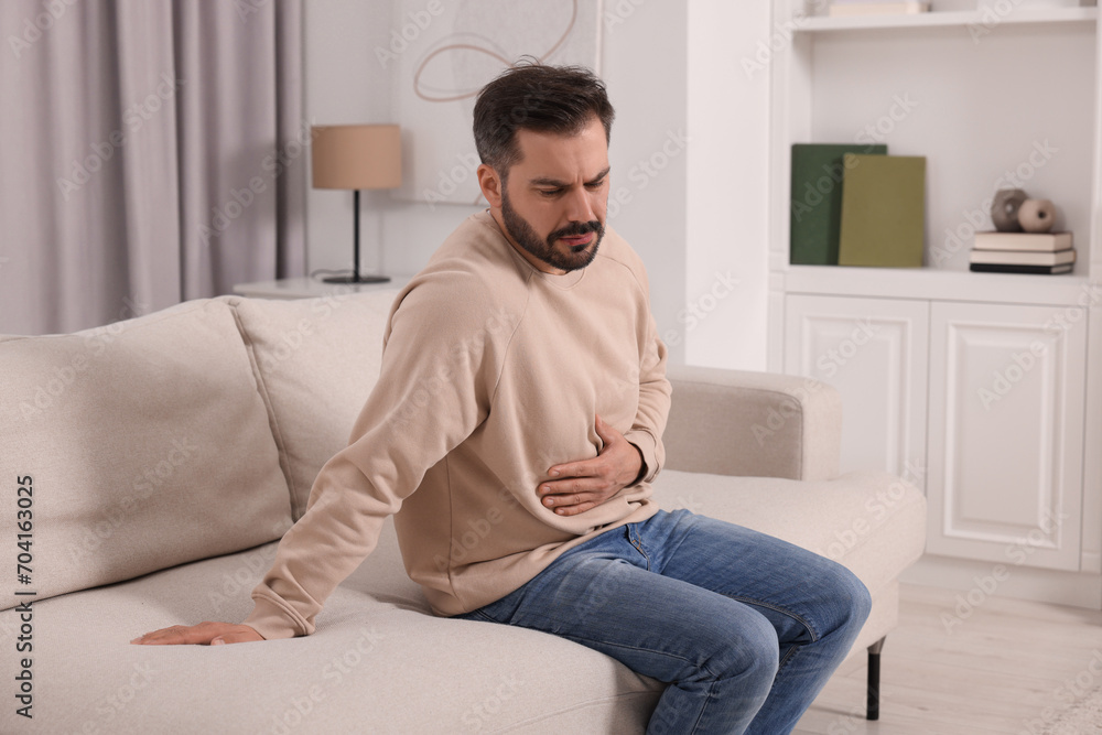 Unhappy man suffering from stomach pain on sofa at home